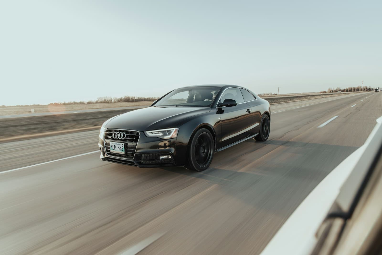 Dark Audi sedan at speed on an empty highway, captured with motion blur