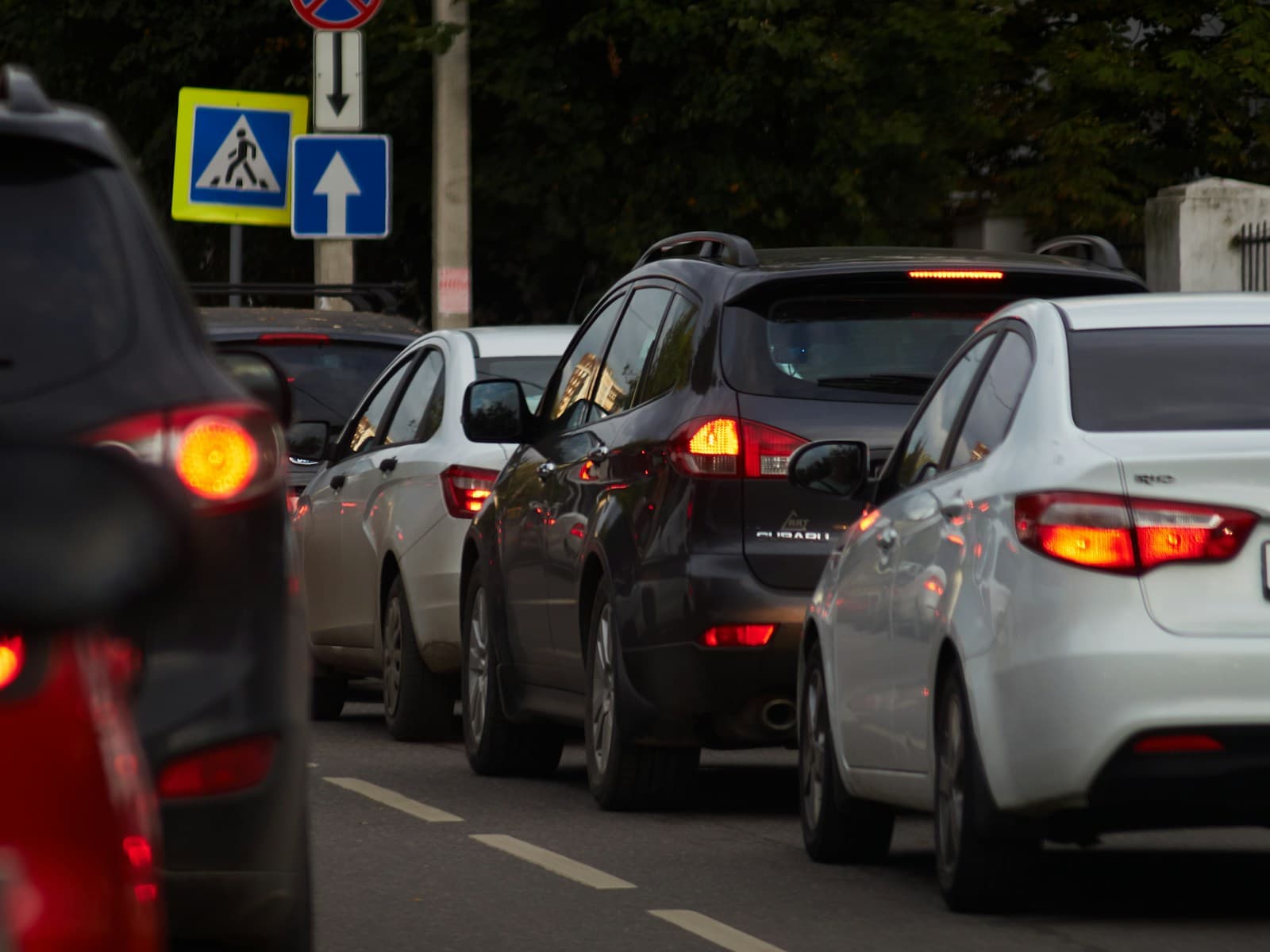 Cars with brake lights on stuck in heavy traffic jam on city street with road signs visible