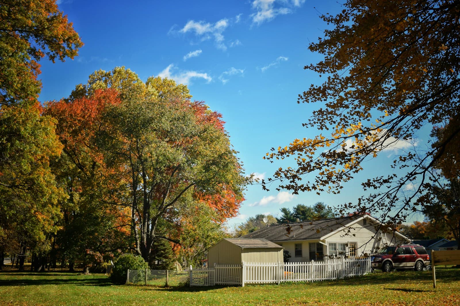 Suburban house with white picket fence surrounded by colorful autumn trees and blue sky
