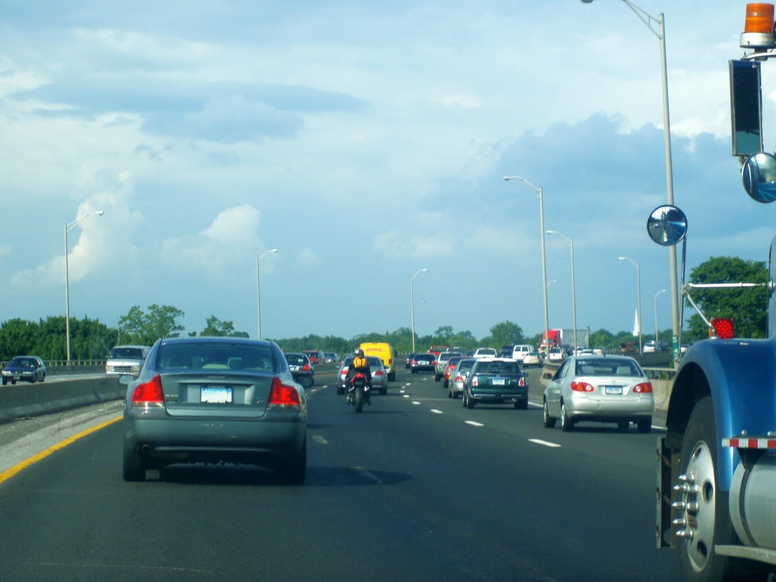 Heavy traffic on a multi-lane highway with cars and trucks in congested lanes under partly cloudy skies