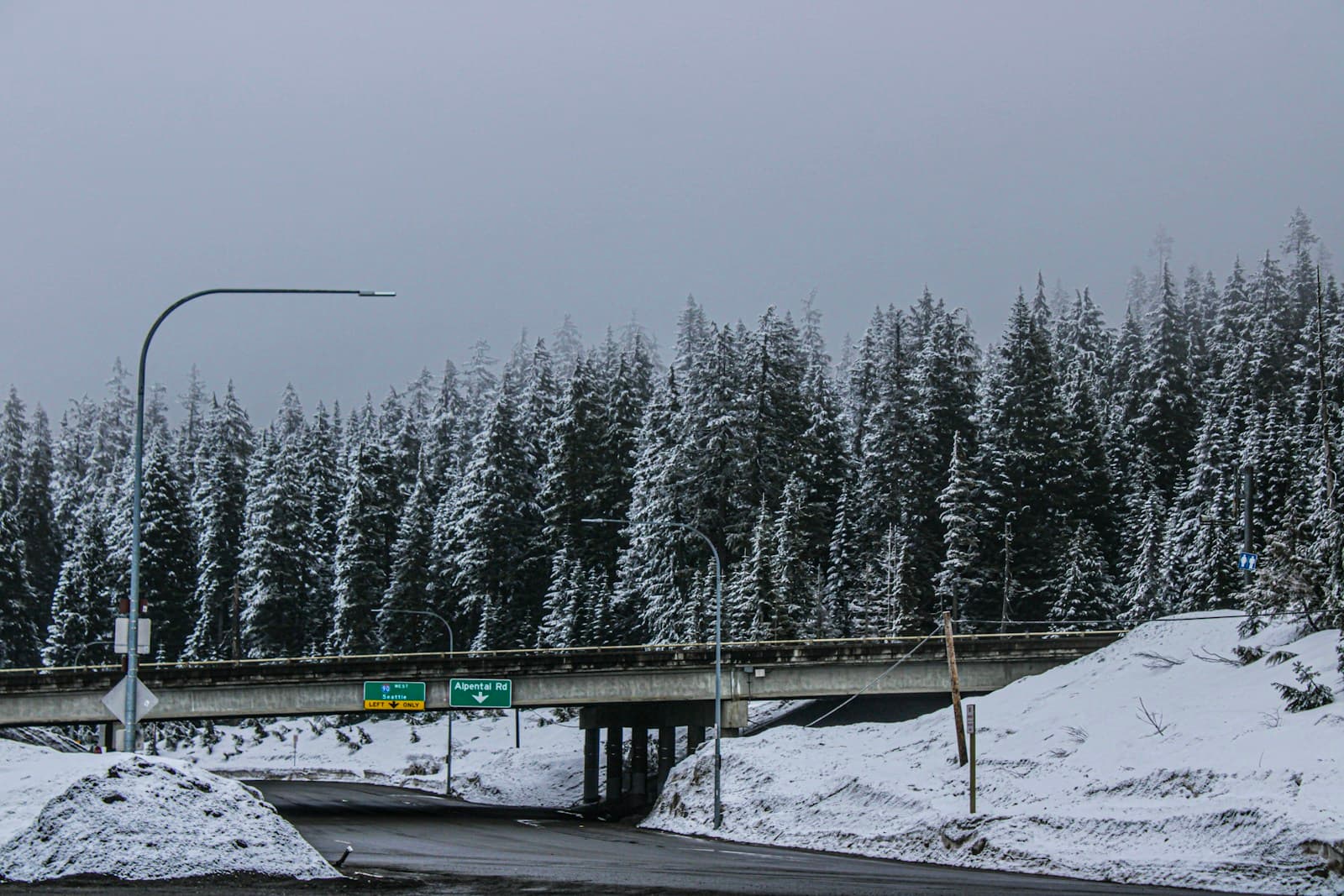 Snow-covered highway overpass with evergreen forest hills behind it in winter