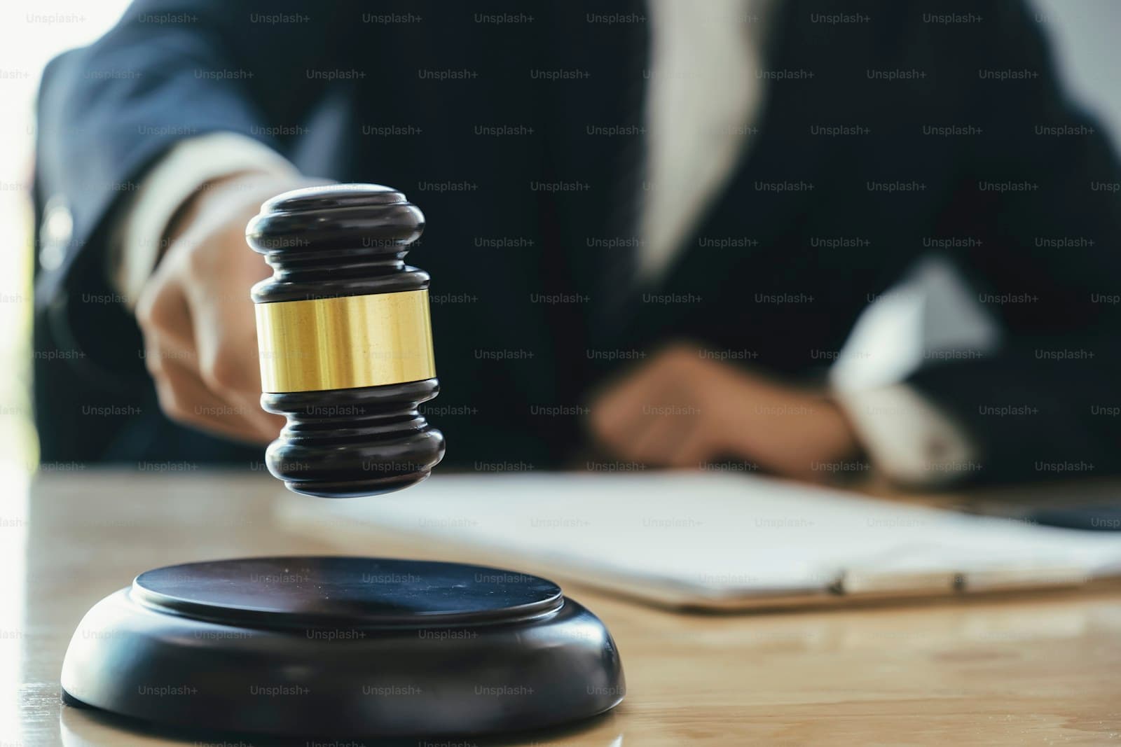 Judge's gavel being held above sound block with blurred person in business suit in background