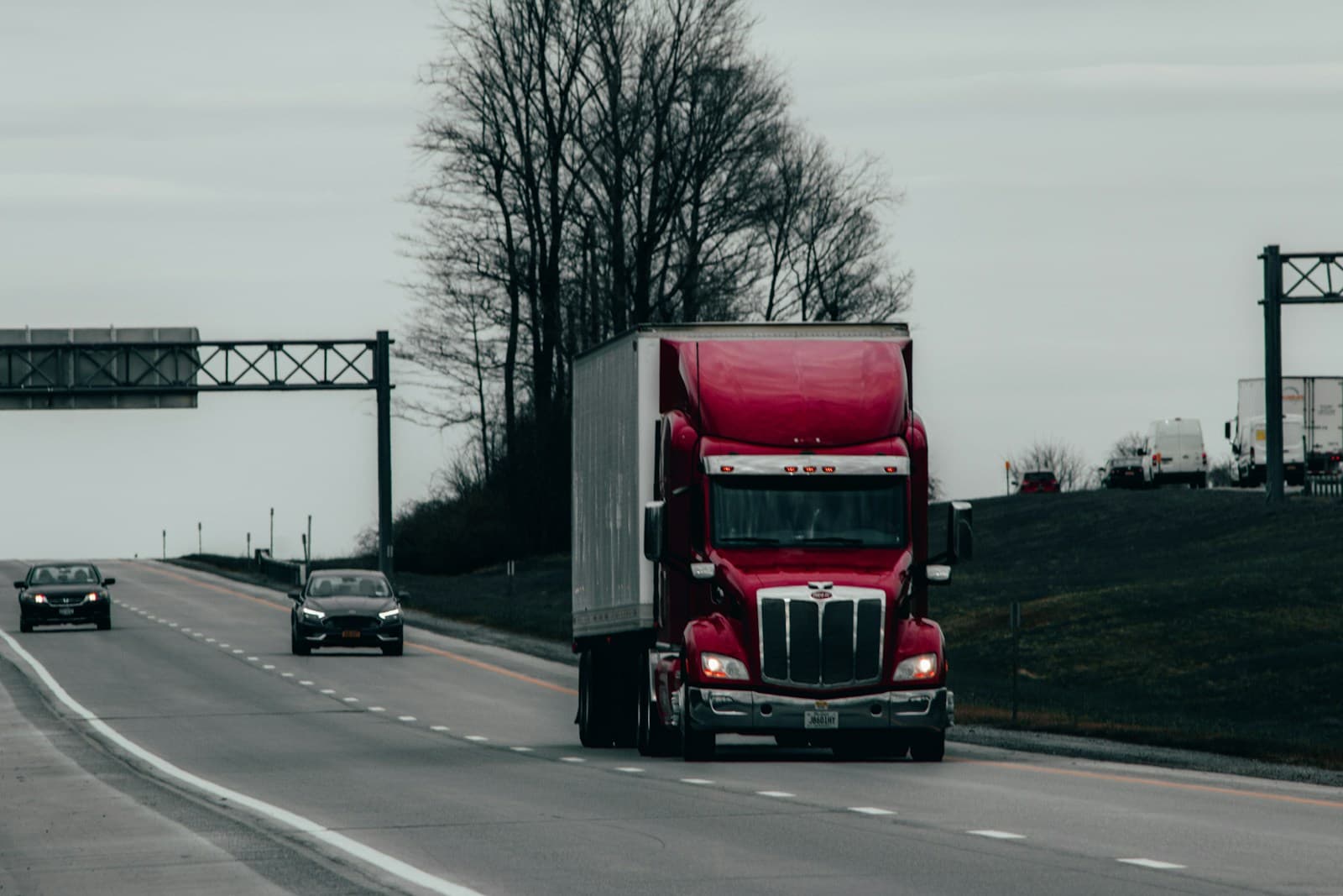 Red semi-truck with a white trailer on a multi-lane highway on an overcast winter day