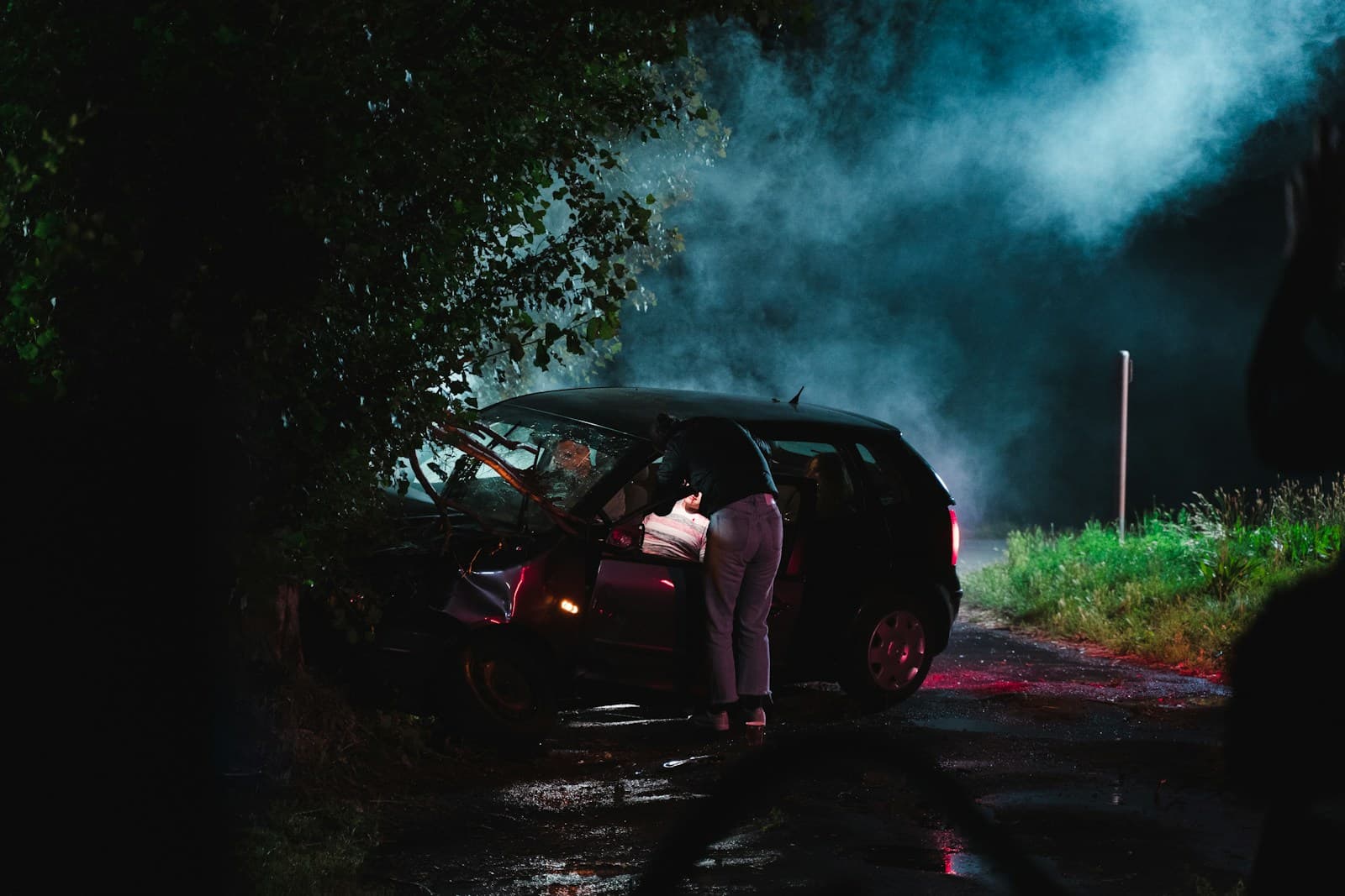 Person standing by car at night with dramatic blue and red lighting on wet road