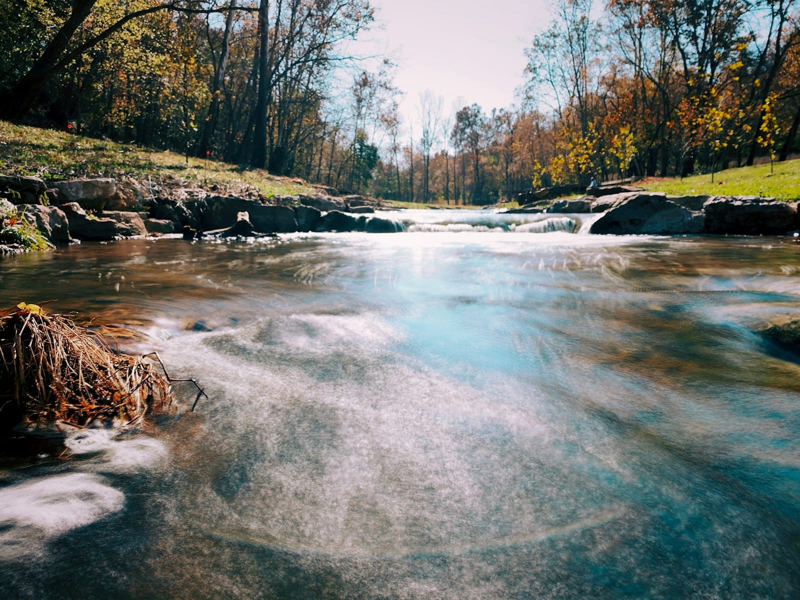 Peaceful stream flowing through autumn forest with golden trees and smooth water captured in long exposure