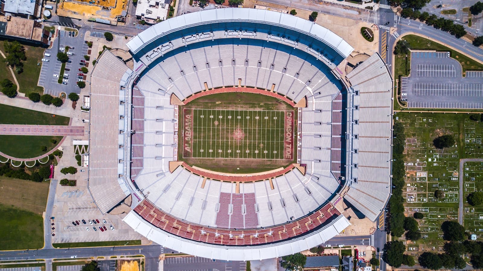 Aerial view of a large football stadium with white exterior and green field surrounded by parking lots