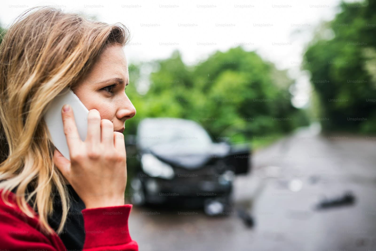 Woman in a red top phoning from the roadside with crashed vehicles behind her