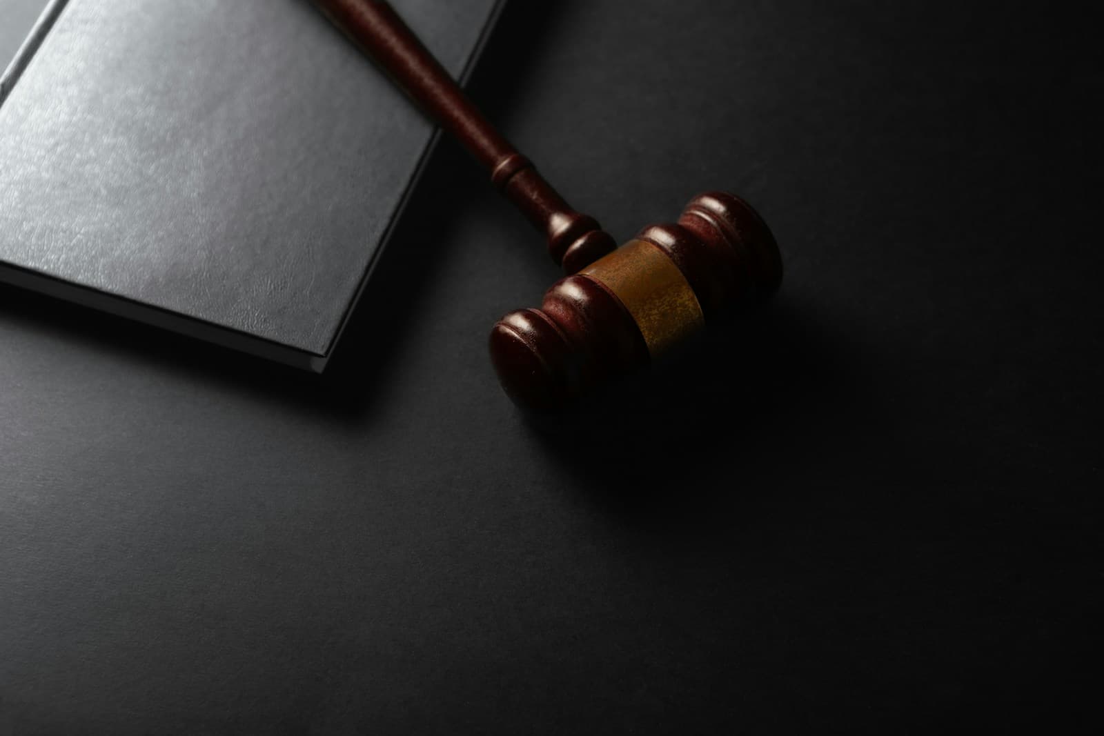 Wooden gavel and black leather book on dark surface representing legal and justice concepts