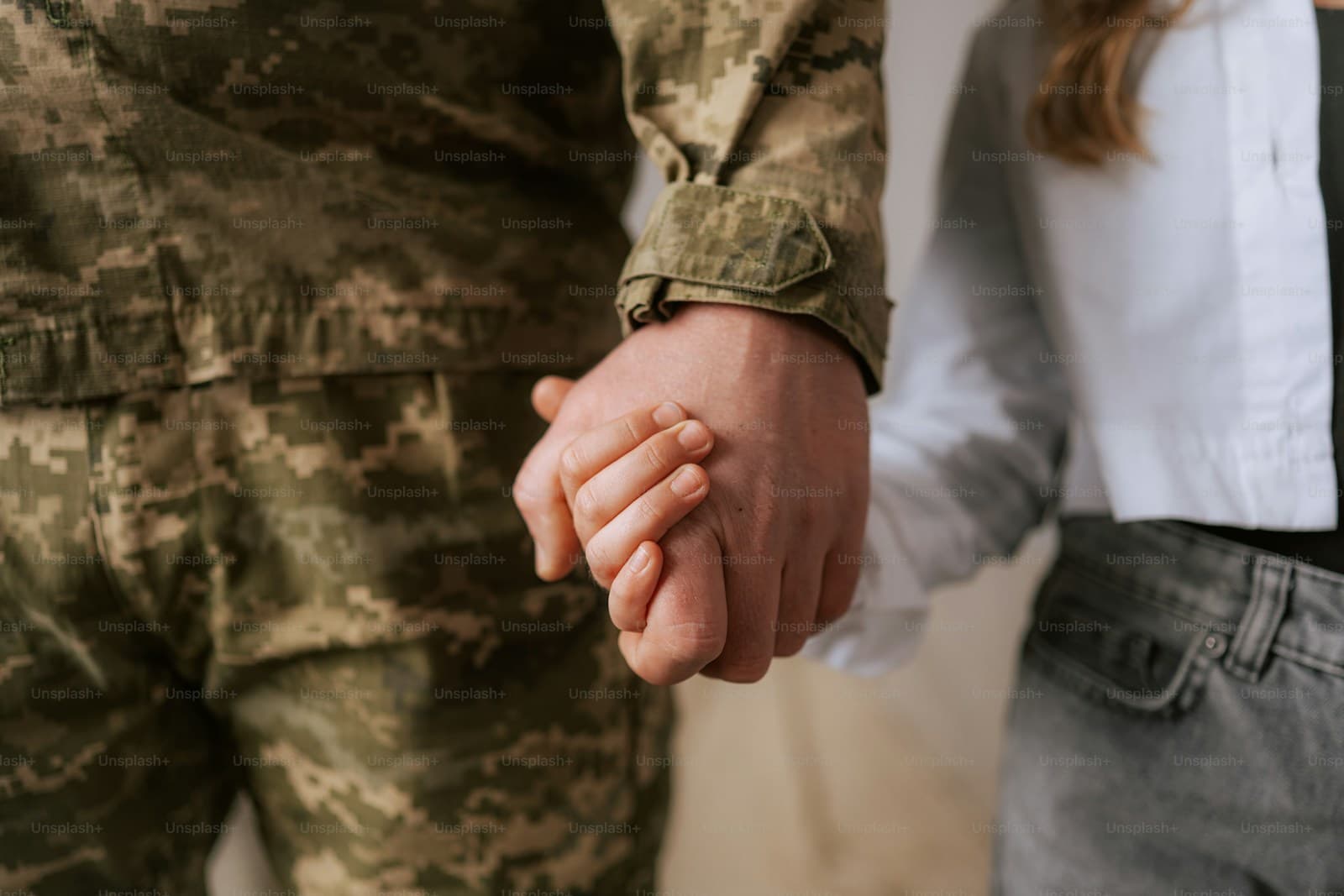 Two people holding hands, one in camouflage uniform and one in civilian clothes