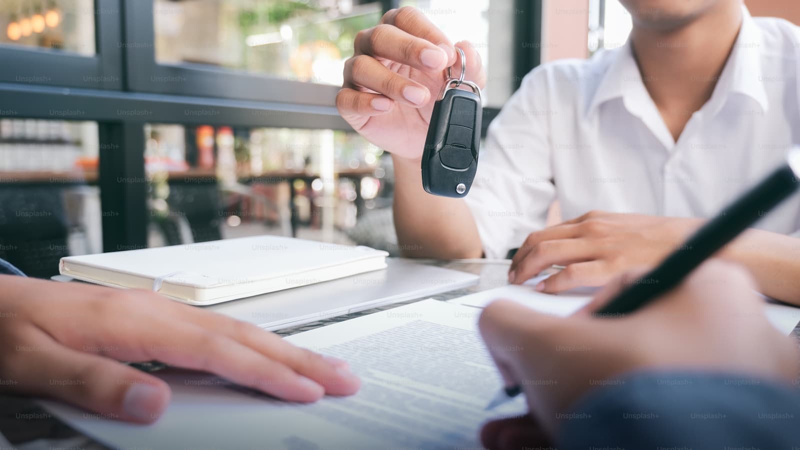 Person handing car keys across desk with paperwork during business transaction