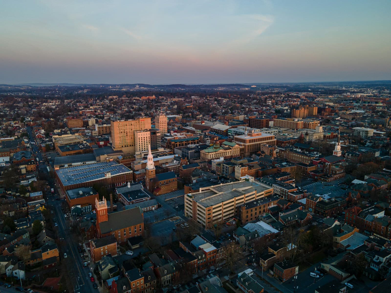 Aerial view of downtown cityscape at sunset with buildings and rolling hills in background