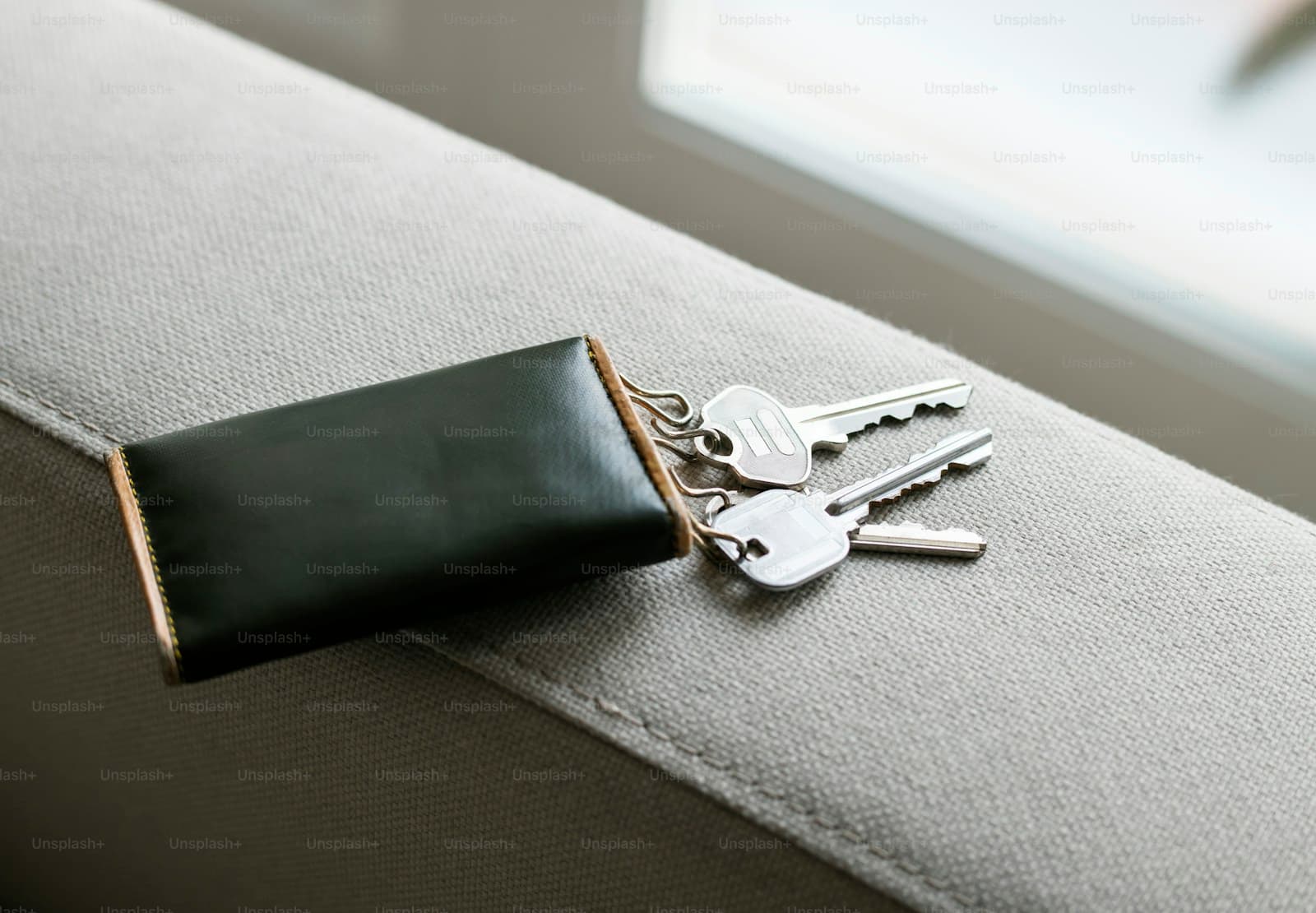 Silver keys with black leather keychain sitting on gray upholstered furniture