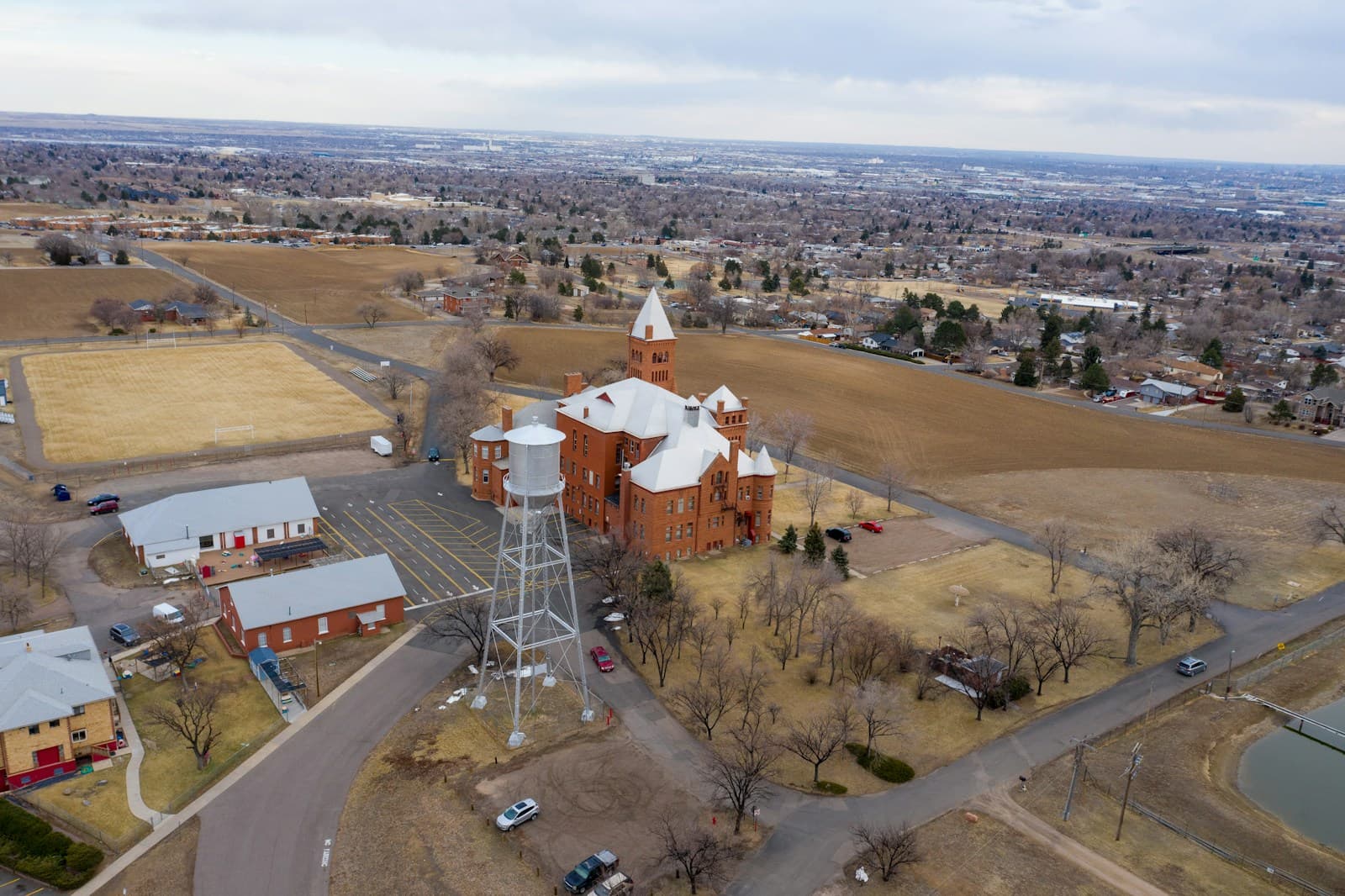 Aerial view of red brick building complex with white water tower in rural setting with farmland and distant hills