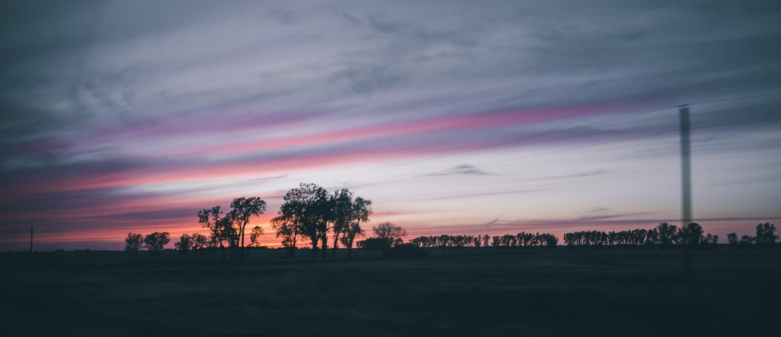 Panoramic sunset landscape with pink and purple sky streaks over silhouetted trees and horizon