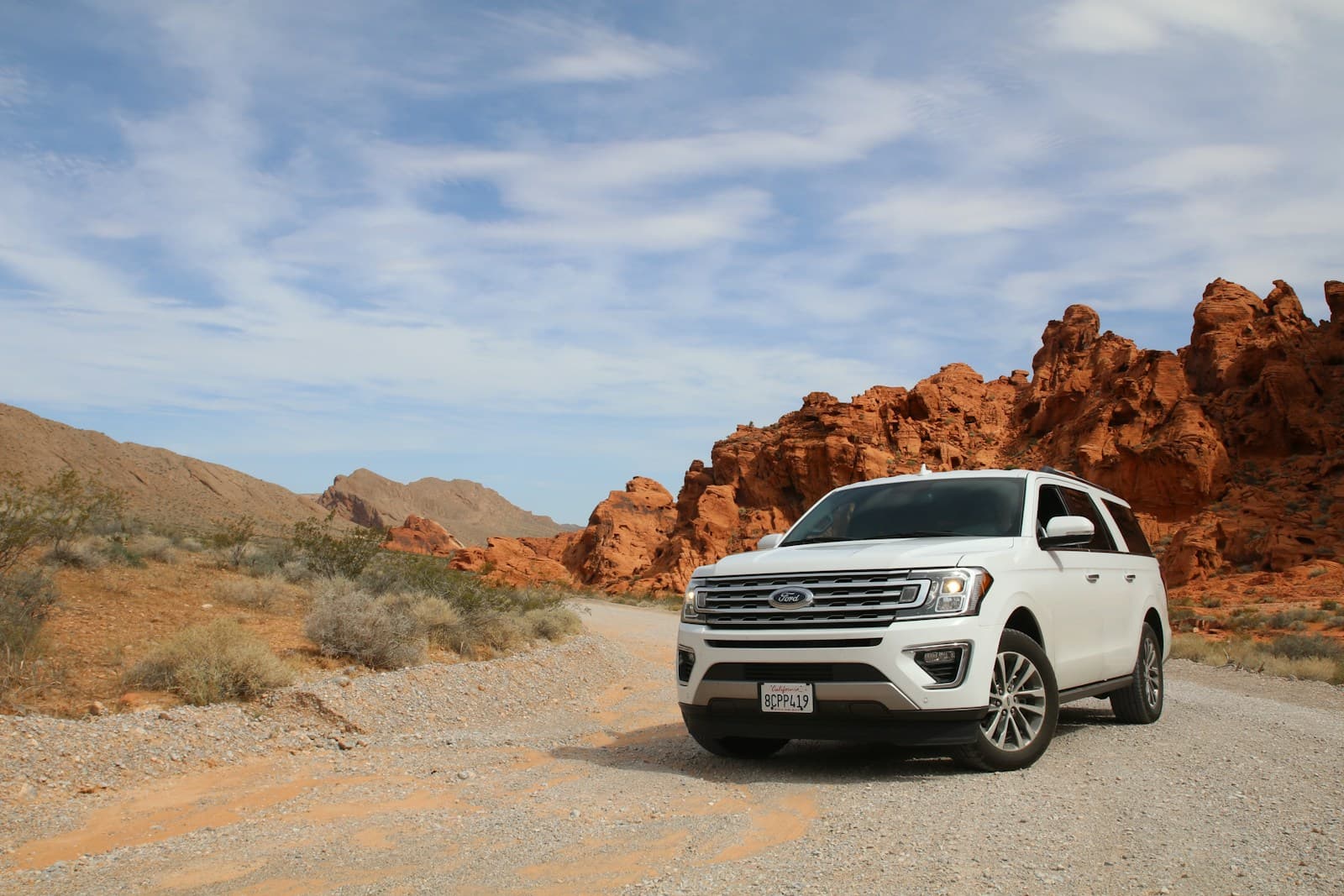 White SUV parked on a desert road below dramatic red rock formations
