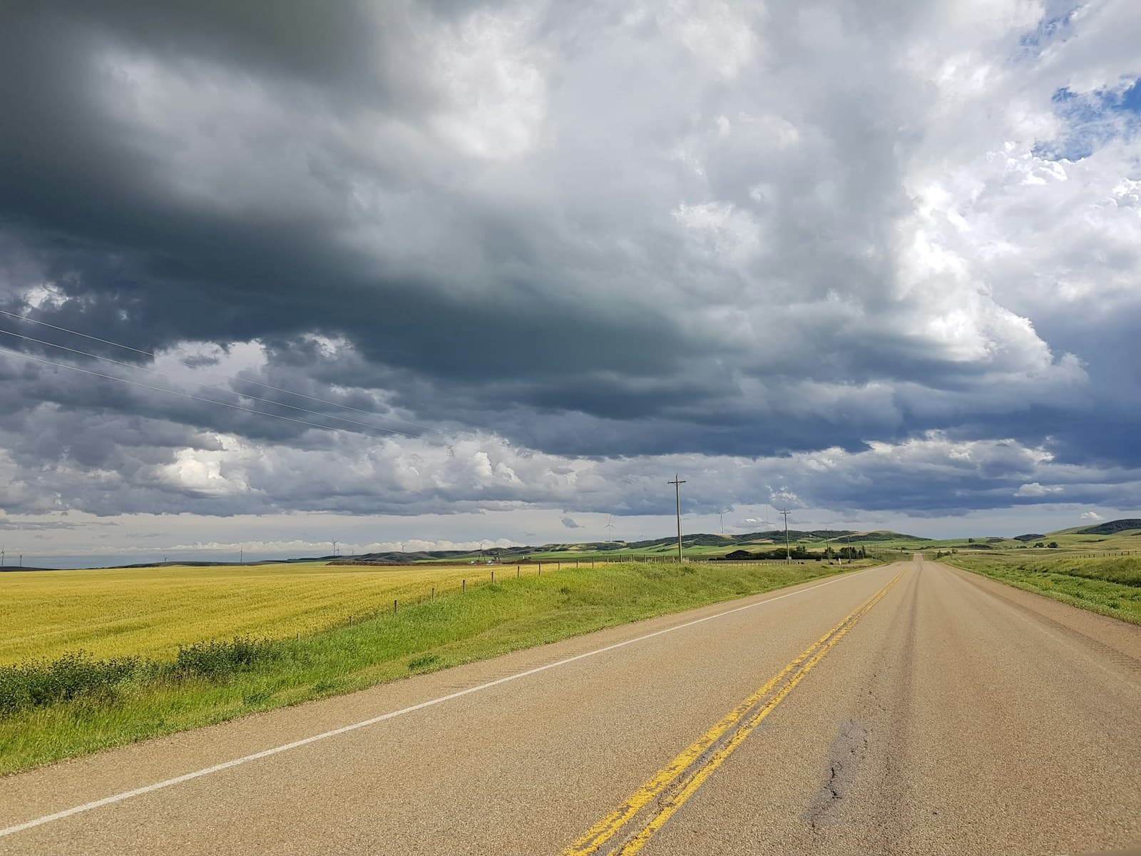 Straight two-lane road crossing golden fields under a dramatic sky
